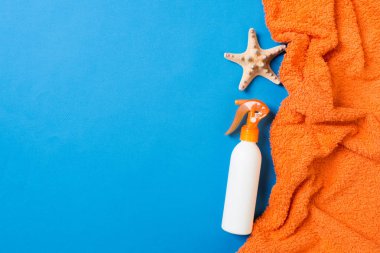 Summer beach flat lay accessories. Sunscreen bottle cream, towel and seashells on colored Background. Travel holiday concept with copy space