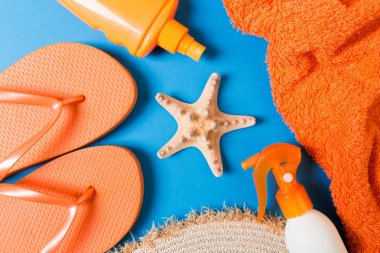 Summer beach flat lay accessories. Sunscreen bottle cream, straw hat, flip flops, towel and seashells on colored Background. Travel holiday concept with copy space