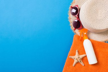 Summer beach flat lay accessories. Sunscreen bottle cream, towel and seashells on colored Background. Travel holiday concept with copy space