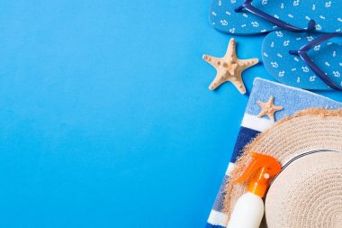 Summer beach flat lay accessories. Sunscreen bottle cream, straw hat, flip flops, towel and seashells on colored Background. Travel holiday concept with copy space