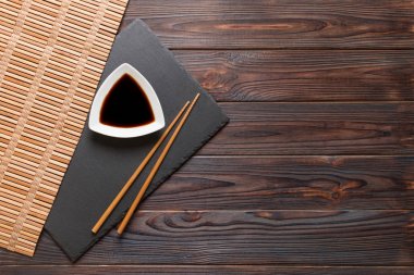 Siyah taş plaka üzerinde chopsticks ve soya sosu, kopya alanı ile ahşap arka plan