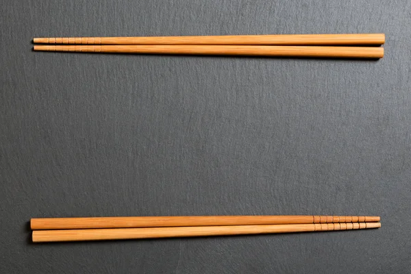 Top view on black slate plate with wooden chopsticks on dark background, copy space — Stock Photo, Image