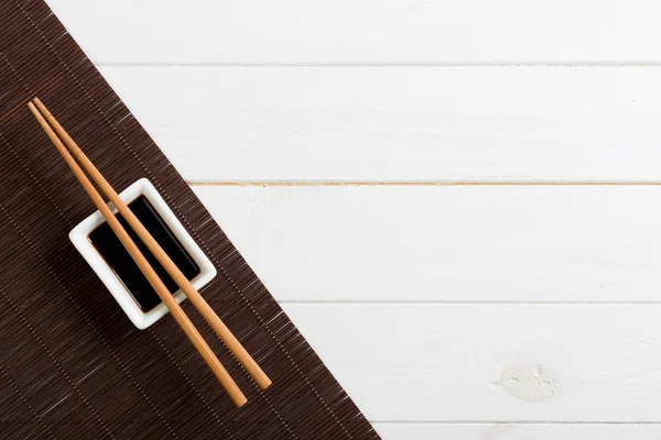 Estera de bambú y salsa de soja con palillos de sushi en la mesa de madera blanca. Vista superior con espacio de copia de fondo para sushi. Puesta plana —  Fotos de Stock