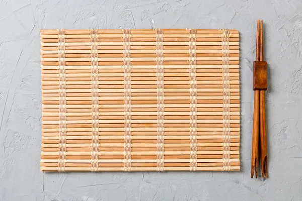 Dva sushi hůlky s prázdnou bambusovou rohoží nebo dřevěnou deskou na kameni pohled shora se stosem — Stock fotografie