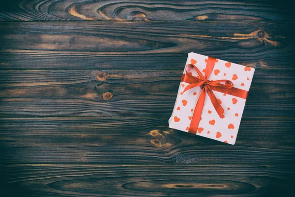 Valentin ou autre cadeau de vacances fait à la main en papier avec des cœurs rouges et une boîte cadeau dans un emballage de vacances. Coffret cadeau sur table en bois sombre vue de dessus avec espace de copie, espace vide pour la conception — Photo