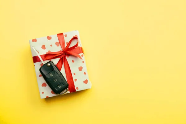 Give gift car key concept top view. Present box with red ribbon bow, heart and car key on yellow colored background