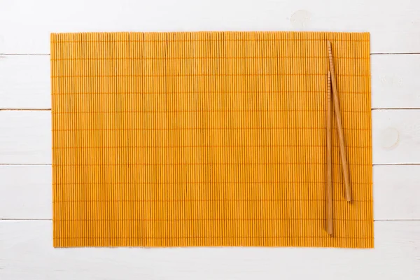 Två sushi ätpinnar med Tom gul bambu matta eller träplatta på vit trä bakgrund uppifrån med kopia utrymme. Töm asiatisk mat bakgrund — Stockfoto
