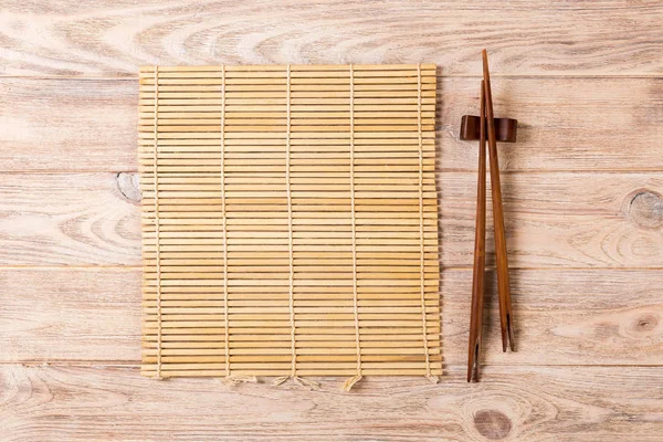 Две палочки суши с пустым коричневым бамбуковым ковриком или деревянной тарелкой на коричневом деревянном фоне Вид сверху с копировальным местом. пустой азиатский продовольственный фон — стоковое фото