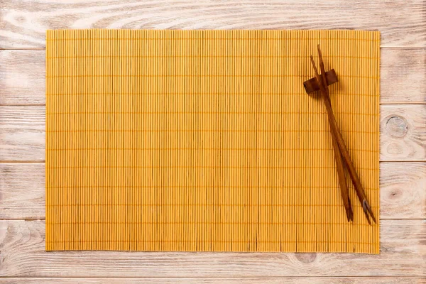 Dois pauzinhos de sushi com esteira de bambu amarelo vazio ou placa de madeira no fundo de madeira marrom Visão superior com espaço de cópia. vazio asiático comida fundo — Fotografia de Stock