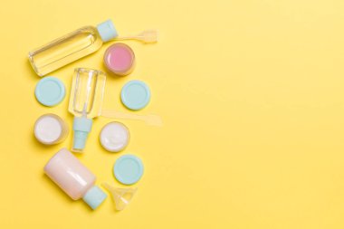 Sarı arka plandaki kozmetik ürünleri için küçük gezici şişelerin ve kavanozların üst görünümü. Tasarımınız için kopya alanı olan yüz bakımı konsepti