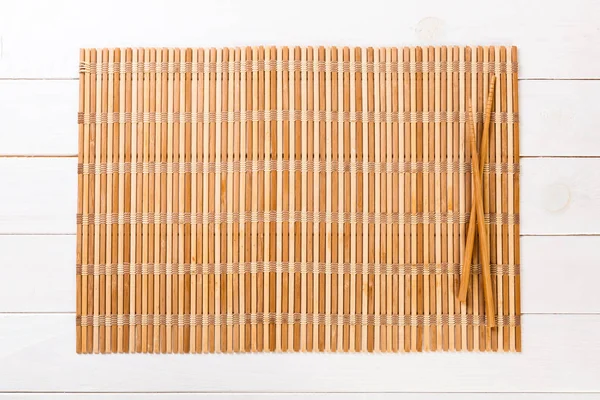 Dva sushi hůlky s prázdnou hnědou bambusovou rohoží nebo dřevěnou deskou na bílém dřevěném pozadí zobrazení top s prostorem pro kopírování. prázdné asijské pozadí jídla — Stock fotografie