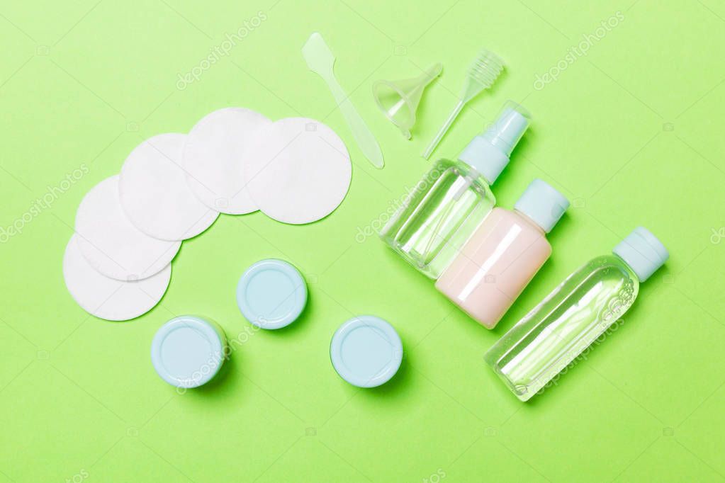 Top view of means for face care: bottles and jars of tonic, micellar cleansing water, cream, cotton pads on green background. Bodycare concept with empty cpace for your ideas
