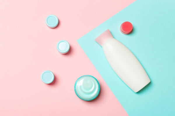 Top view of different cosmetic bottles and container for cosmetics on pink and blue background. Flat lay composition with copy space