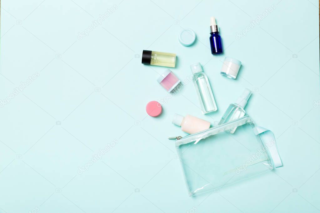 Group of small bottles for travelling on blue background. Copy space for your ideas. Flat lay composition of cosmetic products. Top view of cream containers with cotton pads