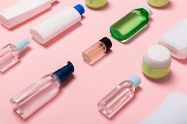 Pembe arka planda kozmetik kaplar, spreyler, kavanoz ve şişeler üst görünümü. Tasarımınız için boş alana sahip yakın çekim görünümü