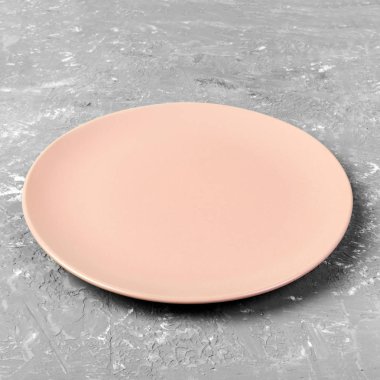 Gri çimento masa arka plan üzerinde boş pembe veya mercan yuvarlak plaka. Üst görünüm, tasarımınız için şablon