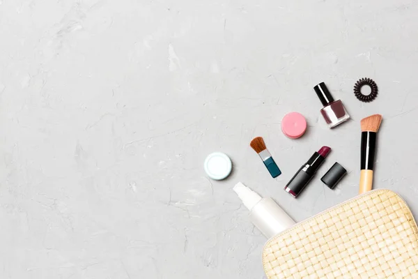 Top view of make up products fallen out of cosmetics bag on cement background. Cosmetic concept with space for your design