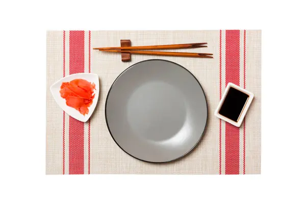 Tom rund grå tallrik med ätpinnar för sushi och sojasås, ingefära på sushimatta bakgrund. Toppvy med kopierings utrymme för dig design — Stockfoto