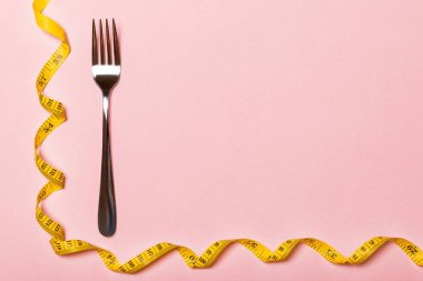 Pembe arka plan üzerinde kıvrılmış bant ölçüsü ile Çatal. Ftatware üst görünümü. Tasarım için alan ile Diyet kavramı