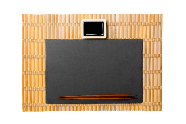 Tom rektangulär svart skiffer tallrik med pinnar för sushi och soja sås på gul bambu matta bakgrund. Toppvy med kopierings utrymme för dig design — Stockfoto