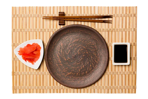 Empty round brown plate with chopsticks for sushi and soy sauce, ginger on yellow bamboo mat background. Top view with copy space for you design — Stock Photo, Image