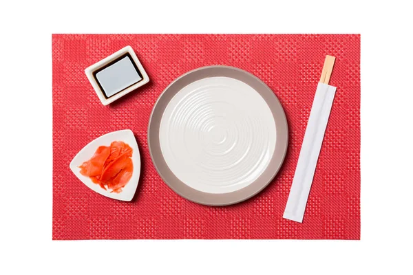 Empty round white plate with chopsticks for sushi and soy sauce, ginger on red mat sushi background. Top view with copy space for you design — Stock Photo, Image