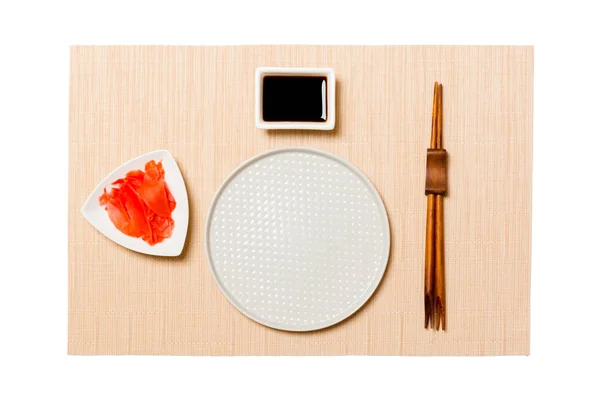 갈색 초밥 매트 배경에 초밥, 생강, 간장 젓가락이 있는 둥근 흰색 접시. 디자인할 복사 공간이 있는 맨 위 뷰 — 스톡 사진