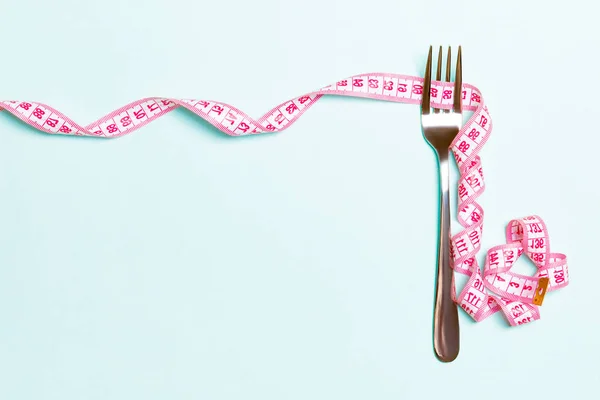 Fork and curled measuring tape are on blue background with top view. Concept of diet for weight loss and space for your design — Stock Photo, Image