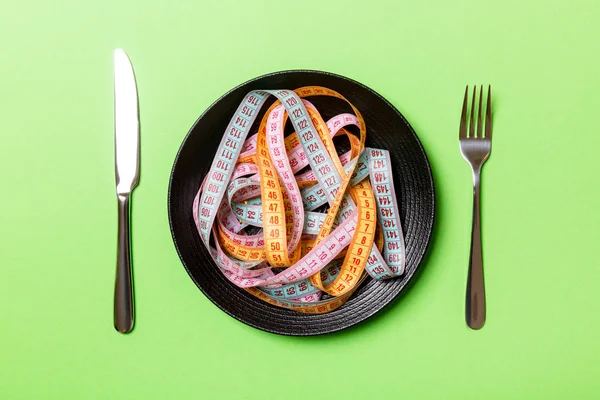 Top view of heap of colorful measuring tapes in plate on green background. Diet concept with copy space — Stock Photo, Image
