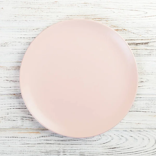 Empty pink or coral round plate on wooden table background. Top view, template for your design