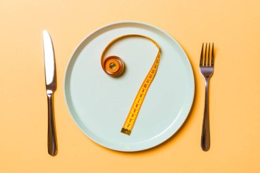 Turuncu arka plan üzerinde yuvarlak plaka üzerinde ölçüm bandı yapılmış soru işareti. Tereddüt ve diyet kavramının en iyi görünümü