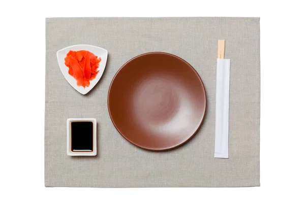 Tom rund brun tallrik med ätpinnar för sushi, ingefära och sojasås på grå servett bakgrund. Toppvy med kopierings utrymme för dig design — Stockfoto
