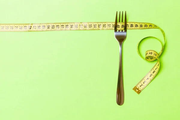 Fork with curled tape measure on green background. Top view of ftatware. Dietary concept with space for your design — Stock Photo, Image
