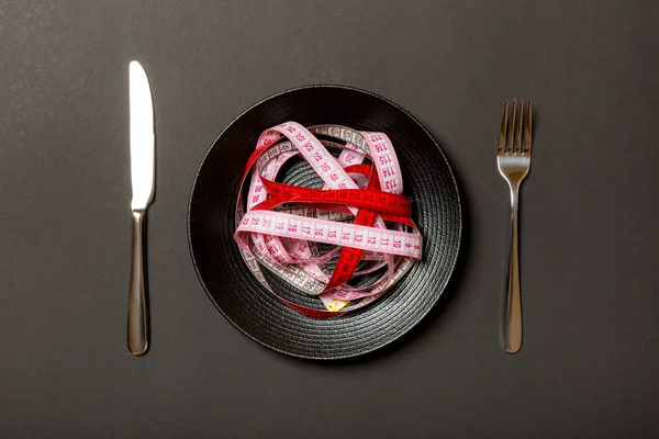 黒い背景に丸いプレートにスパゲッティの代わりにカラフルな測定テープのヒープ。健康的な食事の概念のトップビュー — ストック写真