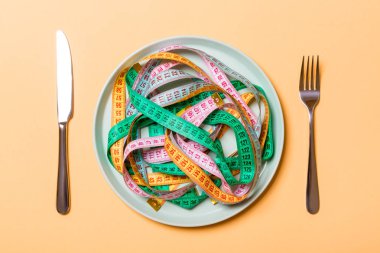 Turuncu arka plan üzerinde bıçak ve çatal ile spagetti şeklinde plaka üzerinde renkli ölçüm bantları üst görünümü. Kilo kaybı ve diyet kavramı