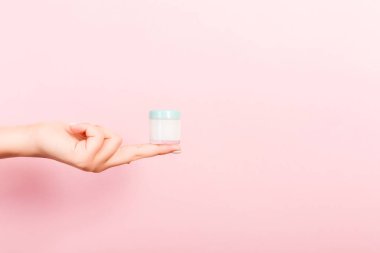 Kadın el tutarak krem şişe losyon izole. Kız pembe arka plan üzerinde kavanoz kozmetik ürünleri vermek