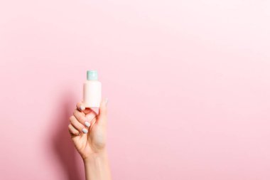 Kadın el tutarak krem şişe losyon izole. Kız pembe arka plan üzerinde tüp kozmetik ürünleri vermek