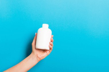 Kadın el tutarak krem şişe losyon izole. Kız mavi arka plan üzerinde tüp kozmetik ürünleri vermek