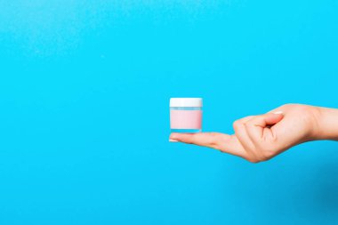 Kadın el tutarak krem şişe losyon izole. Kız mavi arka plan üzerinde kavanoz kozmetik ürünleri vermek