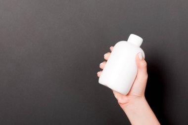 Kadın el tutarak krem şişe losyon izole. Kız siyah arka plan üzerinde tüp kozmetik ürünleri vermek