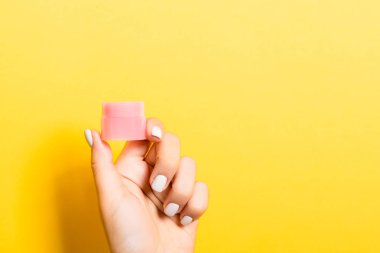 Kadın el tutarak krem şişe losyon izole. Kız sarı arka plan üzerinde kavanoz kozmetik ürünleri vermek