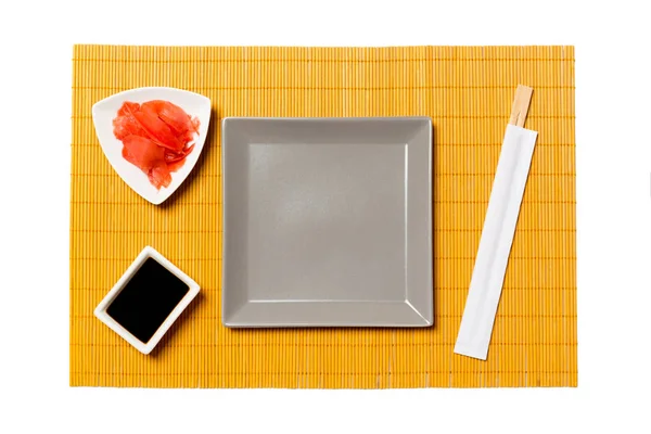 Tom grå fyrkantig tallrik med ätpinnar för sushi, ingefära och sojasås på gul bambu matta bakgrund. Toppvy med kopierings utrymme för dig design — Stockfoto