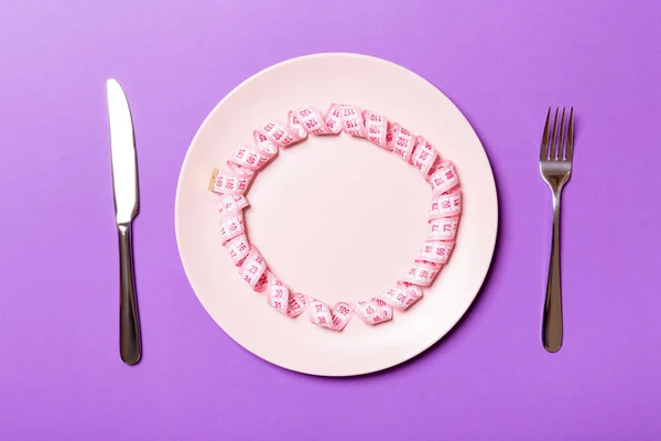 Measuring tape in a plate with fork and knife on both sides on purple background. Top view of weight loss concept — Stock Photo, Image