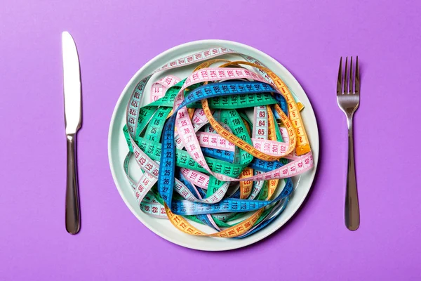 Top view of heap of colorful measuring tapes in plate on purple background. Diet concept with copy space — Stock Photo, Image
