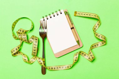 Yeşil arka plan üzerinde tasarım için boş alan ile Fitness konsepti. Sarı ölçü bandı ile çevrili not defteri ve çatalÜst görünümü