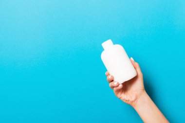 Kadın el tutarak krem şişe losyon izole. Kız mavi arka plan üzerinde tüp kozmetik ürünleri vermek