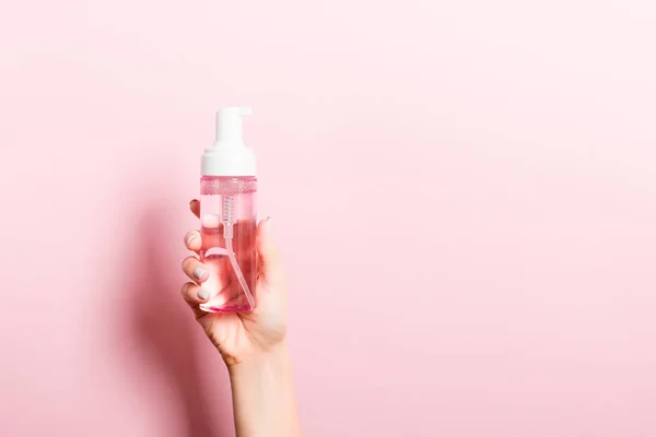 Női kéz tartó spray krém üveg krém izolált. Lány adjon kozmetikai termékek rózsaszín háttér — Stock Fotó