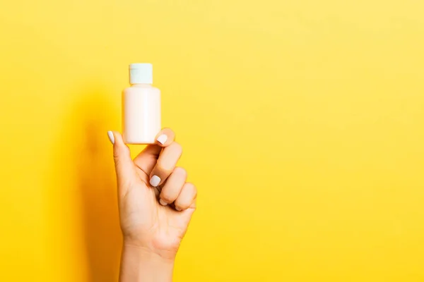 Botella de crema de mano femenina de loción aislada. Chica dar productos cosméticos tarro sobre fondo amarillo —  Fotos de Stock