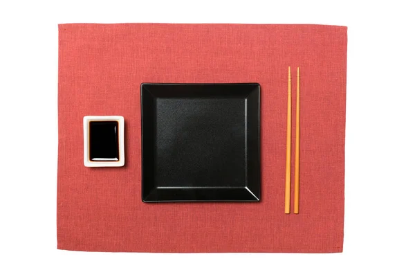 Άδειο μαύρο τετράγωνο πιάτο με ξυλάκια για σούσι και σόγια σάλτσα σε κόκκινο φόντο χαρτοπετσέτα. Κορυφαία προβολή με χώρο αντιγραφής για τη σχεδίασή σας — Φωτογραφία Αρχείου