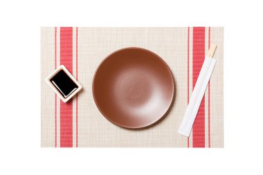 Suşi mat arka plan üzerinde suşi ve soya sosu için çubukları ile Boş yuvarlak kahverengi plaka. Tasarım için kopyalama alanı ile üst görünüm